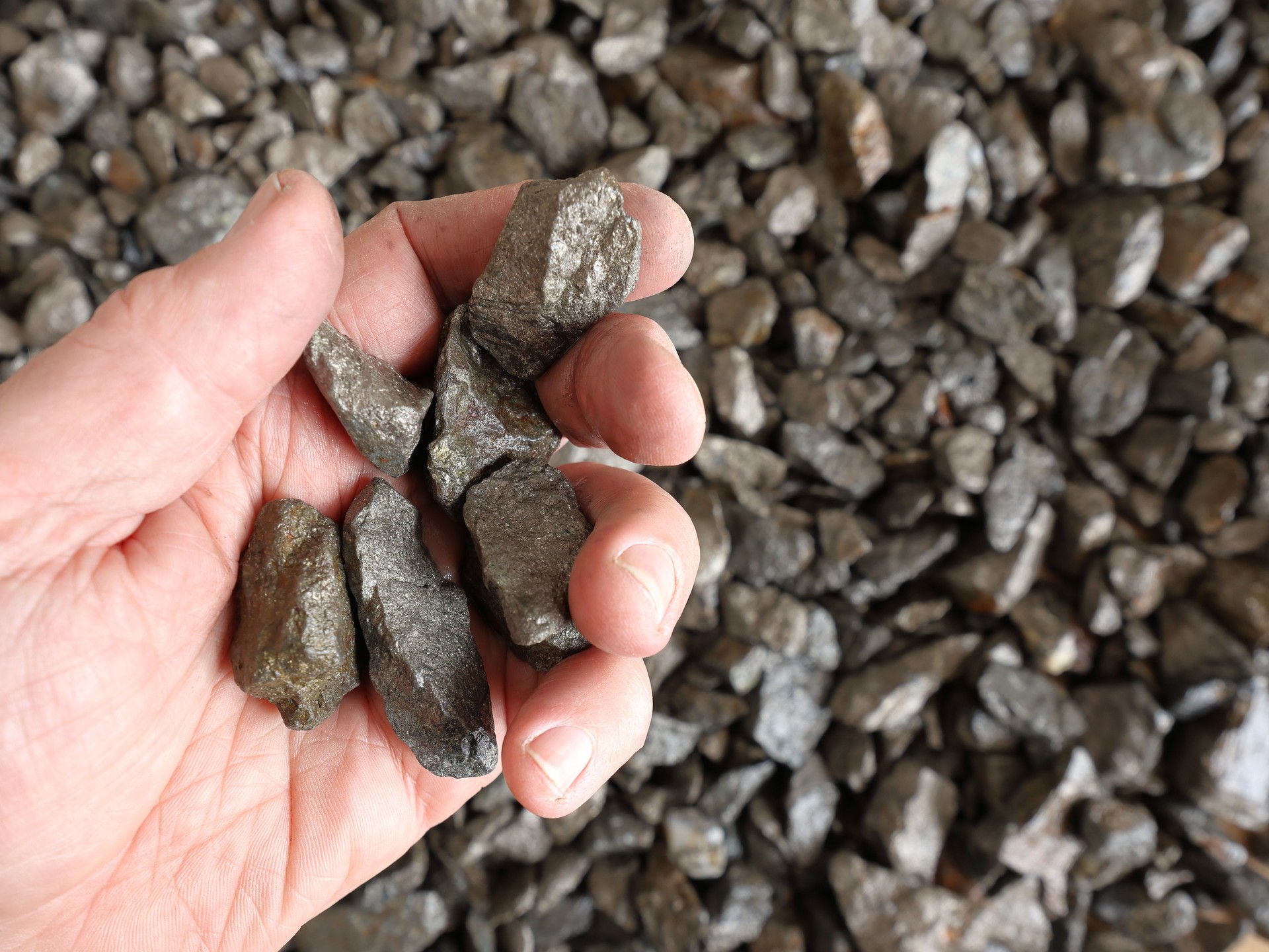 Nickel mine, mining. Hand holding pieces of pentlandite ore. Rocks, textured. Used in alloys such as stainless steel, nickel-cadmium rechargeable batteries, coins